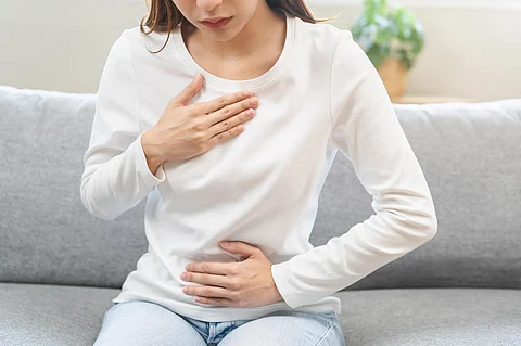 Enfermedad de reflujo ácido, sufre una mujer joven asiática que tiene síntomas gastroesofágicos, esofágicos, dolor de estómago y dolor de acidez estomacal con la mano en el pecho por un problema de digestión después de comer alimentos, concepto médico de atención médica