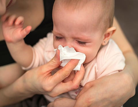 A small, sick, crying child, whom the mother wipes with a paper towel
