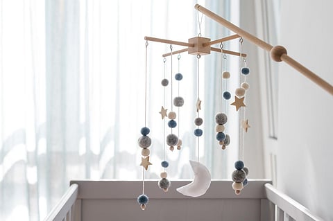 Cuna móvil para bebés con estrellas, planetas y luna. Juguetes hechos a mano para niños encima de la cuna del recién nacido. Primeros juguetes ecológicos para bebés hechos de fieltro y madera colgados en una habitación iluminada. Espacio para el texto.
