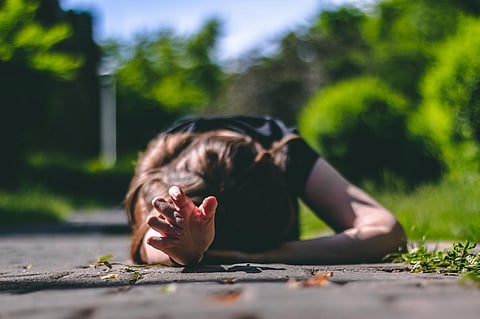 Mujer joven con cabello castaño con una camiseta negra acostada en un callejón del parque con una mano buscando ayuda â Imagen conceptual para epilepsia, ataque cardíaco o enfermedad
