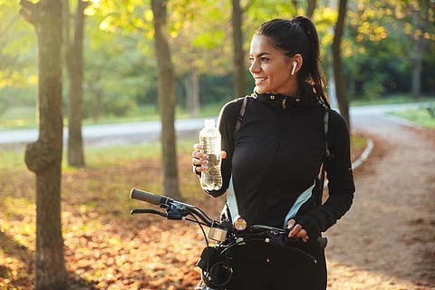 Mujer con una bicicleta en el parque, bebiendo agua de una botella