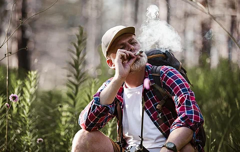Hombre maduro barbudo fumando marihuana medicinal en la naturaleza.
