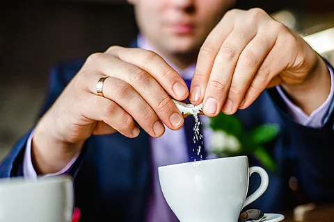 Man sweetening his drink. groom pours sugar in coffee