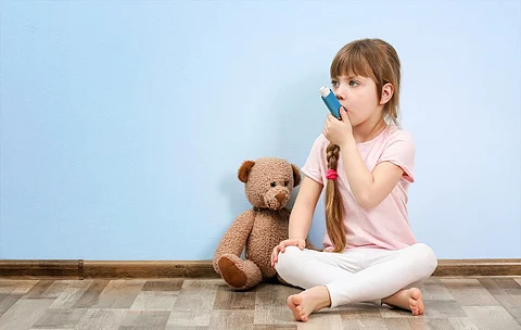 Linda niña sentada en el suelo mientras usa el inhalador. Concepto de alergia