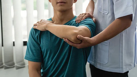Man physiotherapist assisting male patient with elbow injury at clinic.