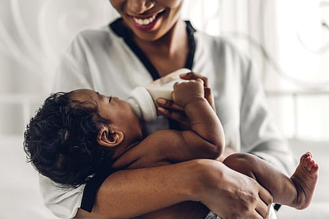 Retrato de disfrutar del amor feliz familia madre afroamericana jugando con adorable bebé afroamericano. Mamá alimentando con biberón de leche a un lindo hijo en una habitación blanca. Concepto de amor por la familia negra