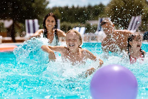 Ball in pool. Cheerful happy parents and children laughing while playing ball in swimming pool