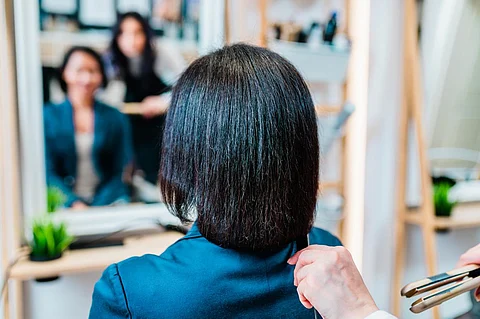 An middle aged African American woman on a curly hair straightening treatment at a hair salon.
