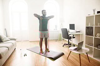 Healthy life. Full length shot of male fitness instructor showing exercises with resistance band, streaming, broadcasting video lesson on training at home using laptop. Sport, online gym concept