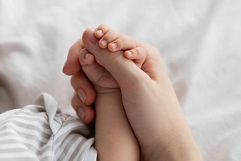Protección de la madre. Primer plano de una madre irreconocible sosteniendo la pequeña mano de su bebé recién nacido mientras se relajan juntos en la cama en casa, disfrutando de la vinculación con el niño pequeño, imagen recortada