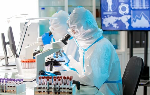 microbiologist biotechnology researcher or medical worker team look microscope in the lab with isolation gown or protective suits and surgical face mask