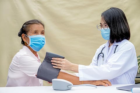 La mujer médica evalúa al paciente anciano con monitor de presión arterial, registra los resultados y guía la atención médica amigable en el hospital de campaña.