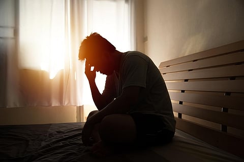 hombre desesperado en silueta sentado en la cama con las manos en la cabeza, dolor de cabeza después de debilitarse