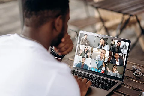 Video call. Online business meeting. Successful African American freelancer communicate by a video conference with his colleagues using a laptop while sitting in cafe in a summer terrace, they discussing about business affairs. On a laptop screen, participants of a video conference