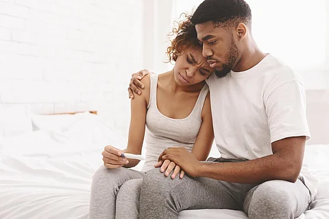 Problema de infertilidad. Pareja afroamericana molesta sentada en la cama con resultado negativo de la prueba de embarazo, espacio libre