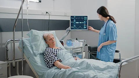 Asistente médico que visita a un paciente jubilado durmiendo en la cama de la sala de hospital. Mujer trabajando como enfermera controlando el monitor de frecuencia cardíaca para la medición del pulso. Especialista en el cuidado de la persona