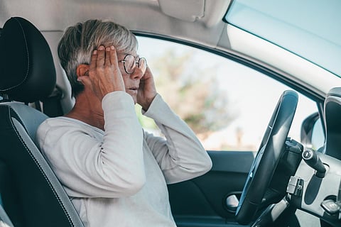 Una mujer mayor o madura que tiene y siente un fuerte dolor de cabeza en el automóvil mientras conduce. Sentir dolor al conducir en carretera
