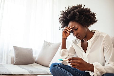 Shot of a young woman looking at the results on her pregnancy test. I can't be pregnant now. Sad and worried woman with a pregnancy test on bed. Woman holding pregnancy test