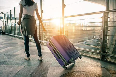Young woman pulling suitcase in airport terminal. Copy space