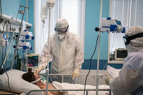 A doctor in a protective suit puts a respiratory mask on a patient with a coronavirus infection Covid-19, who is in the intensive care unit of a modern hospital.