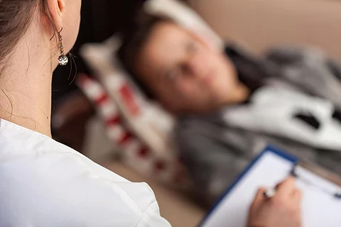 Young teenager boy at psychotherapy, lying on a sofa while counseling professional takes notes - close up, focus on foreground