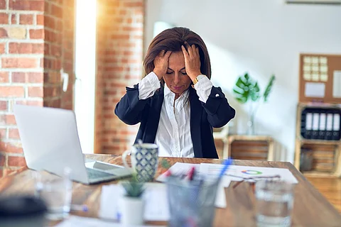 Middle age beautiful businesswoman working using laptop at the office suffering from headache desperate and stressed because pain and migraine. Hands on head.