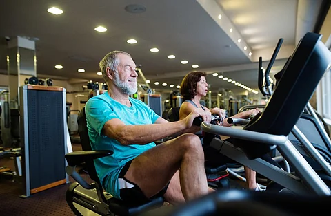 Hermosa pareja mayor en forma con ropa deportiva en el gimnasio haciendo ejercicio cardiovascular, haciendo ejercicio en bicicleta reclinada. Concepto de fitness deportivo y estilo de vida saludable.