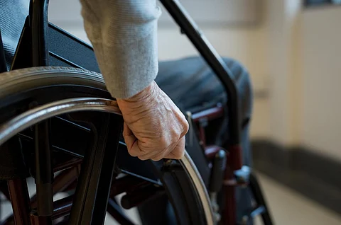 Anciano paralizado usando su silla de ruedas. Primer plano de la mano de un hombre discapacitado empujando la rueda de la silla de ruedas. Detalle de la mano de un hombre mayor sosteniendo la rueda de la silla de ruedas.