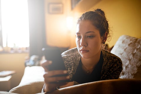 Retrato de una joven adolescente usando el móvil mientras está tumbada en la cama.