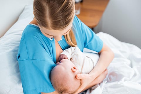 young mother breastfeeding baby on bed in hospital room