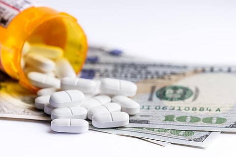 close up of a prescription bottle with white tables falling out on top of a group of hundred dollar bills