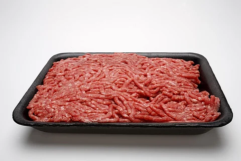 Raw ground beef in black styrofoam container on white background