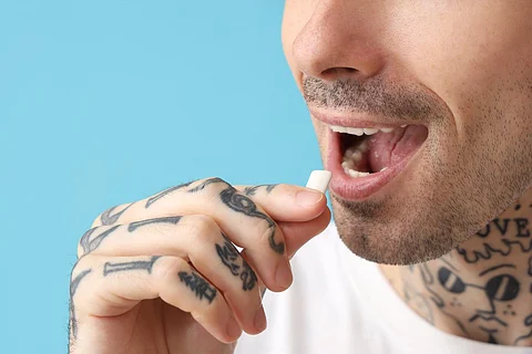 Joven hombre tatuado con chicle sobre fondo azul, primer plano