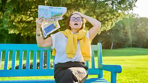 Síntomas de menopausia en una mujer madura, la mujer agita el periódico para refrescarse, siente calor, cambios hormonales de edad. Mujer en el banco del parque