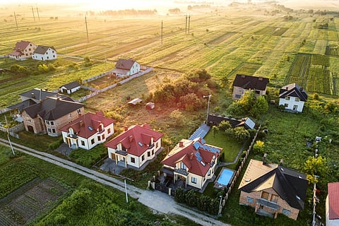 Vista aérea de una zona residencial rural con casas privadas entre campos verdes al amanecer.