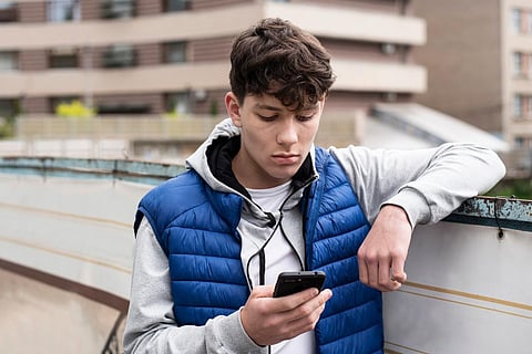 A teenage boy looking into a phone with a sad face and having negative emotions because he read the bad news. The guy is walking in the city and waiting for his friends