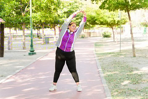 Latin big size woman stretching before running on the track park. Relaxed active woman doing warm up exercises outdoors