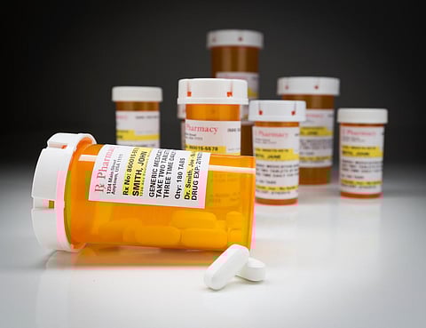 Variedad de frascos de medicamentos no patentados y píldoras grandes sobre superficie reflectante con fondo gris.