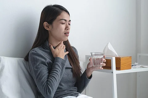 Dolor de garganta en la temporada de gripe. Joven asiática tocándose el cuello y sintiendo dolor en la garganta en el dormitorio de su casa.