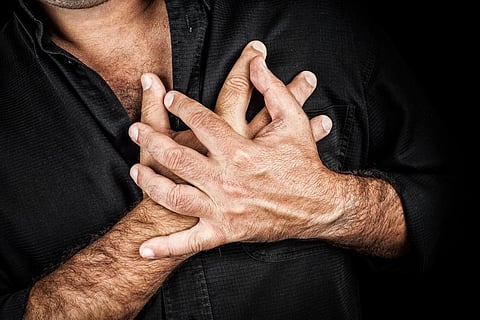 Primer plano de dos manos agarrando un pecho sobre un fondo negro, útil para representar un infarto o cualquier concepto sentimental