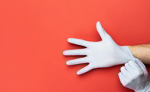 Photo of a person's hands putting on gloves against a red background