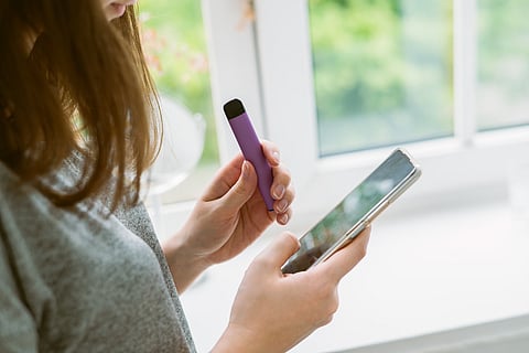 Woman in grey t-shirt holding a purple vape and cellphone
