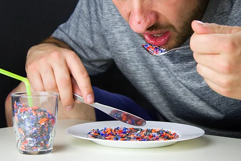 El hombre come pedazos de plástico reciclado triturado de un plato blanco. Los alimentos y bebidas contienen plásticos. Un vaso lleno de plástico reciclado y un plato blanco de piezas de plástico.