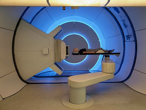 Radioterapia con protones. Paciente infantil con cáncer cerebral acostada en la cama de posicionamiento con máscara de fijación en la cabeza