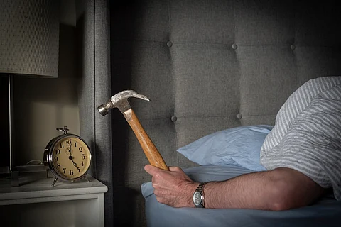 Persona durmiendo en la cama a punto de golpear su despertador matutino con un martillo.