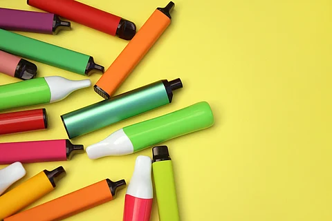 Conjunto de cigarrillos electrónicos desechables multicolor sobre fondo amarillo brillante.