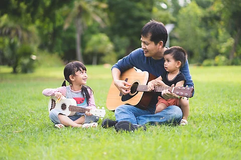 Padre e hija asiáticos tocan la guitarra y el ukelele juntos y el bebé está sentado con ellos, concepto de música y actividad al aire libre para niños en el estilo de vida familiar