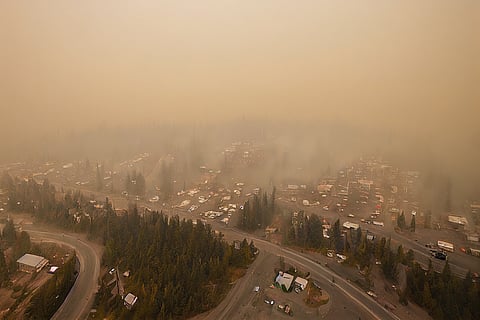 Toma aérea de alto ángulo de un dron de una pequeña ciudad en Canadá que se desvanece lentamente debido al denso humo de los incendios forestales cercanos en el interior de la parte baja de la Columbia Británica. El tráfico y los peatones se ven a continuación.