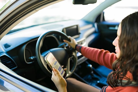 Adolescente conduciendo un automóvil mientras sostiene y usa un teléfono inteligente, lo que representa la conducción distraída y los problemas de seguridad vial