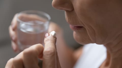 Primer plano de una mujer enferma madura que tiene una píldora de aspirina antibiótica que sufre de dolor de cabeza o migraña, una mujer mayor enferma toma una dosis diaria de vitamina o suplemento, medicamentos, concepto de atención médica para ancianos